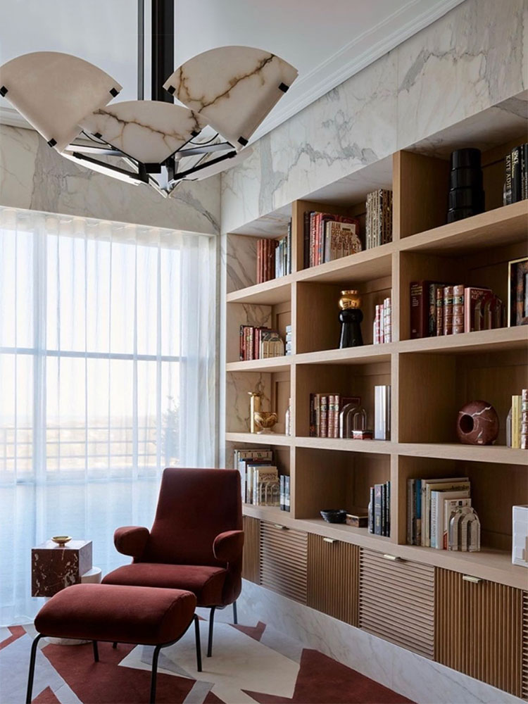 Quart-de-rond-ceiling-lamp | rewire Red upholstered lounge chair with matching ottoman beside a large window, in front of a tall wooden bookshelf and marble walls.