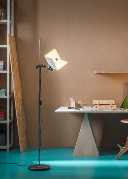 Image of a modern Triedro Floor Lamp with a contoured metal lampshade made of three parts. The lamp features a double joint that allows the light source to be rotated and adjusted flexibly. Available in white, black, or chrome finish.