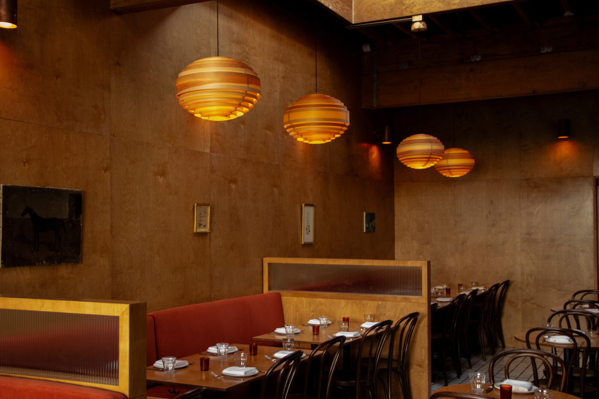A warm restaurant interior with wood walls and bent wood pendant lights