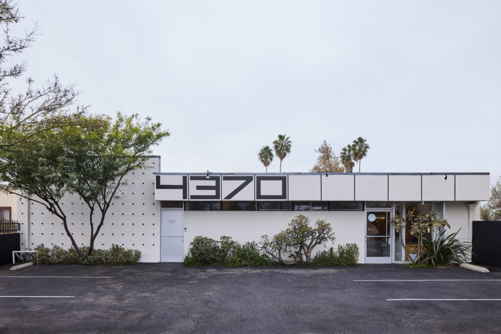 Darnold_112624_rewire_003 - rewire simple black and white building with small parking lot and large 4370 numbers on bulkhead with simple desert landscaping and palm trees in the distance