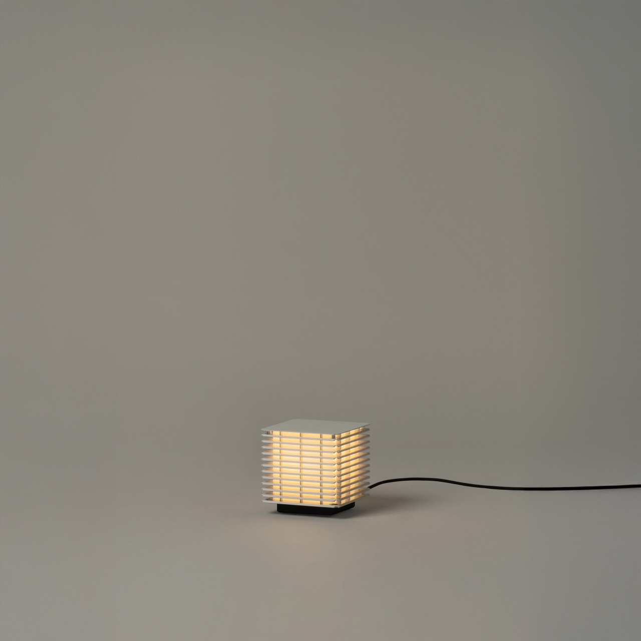 1 | rewire Small square lamp with horizontal slats emitting a warm glow on a neutral surface.