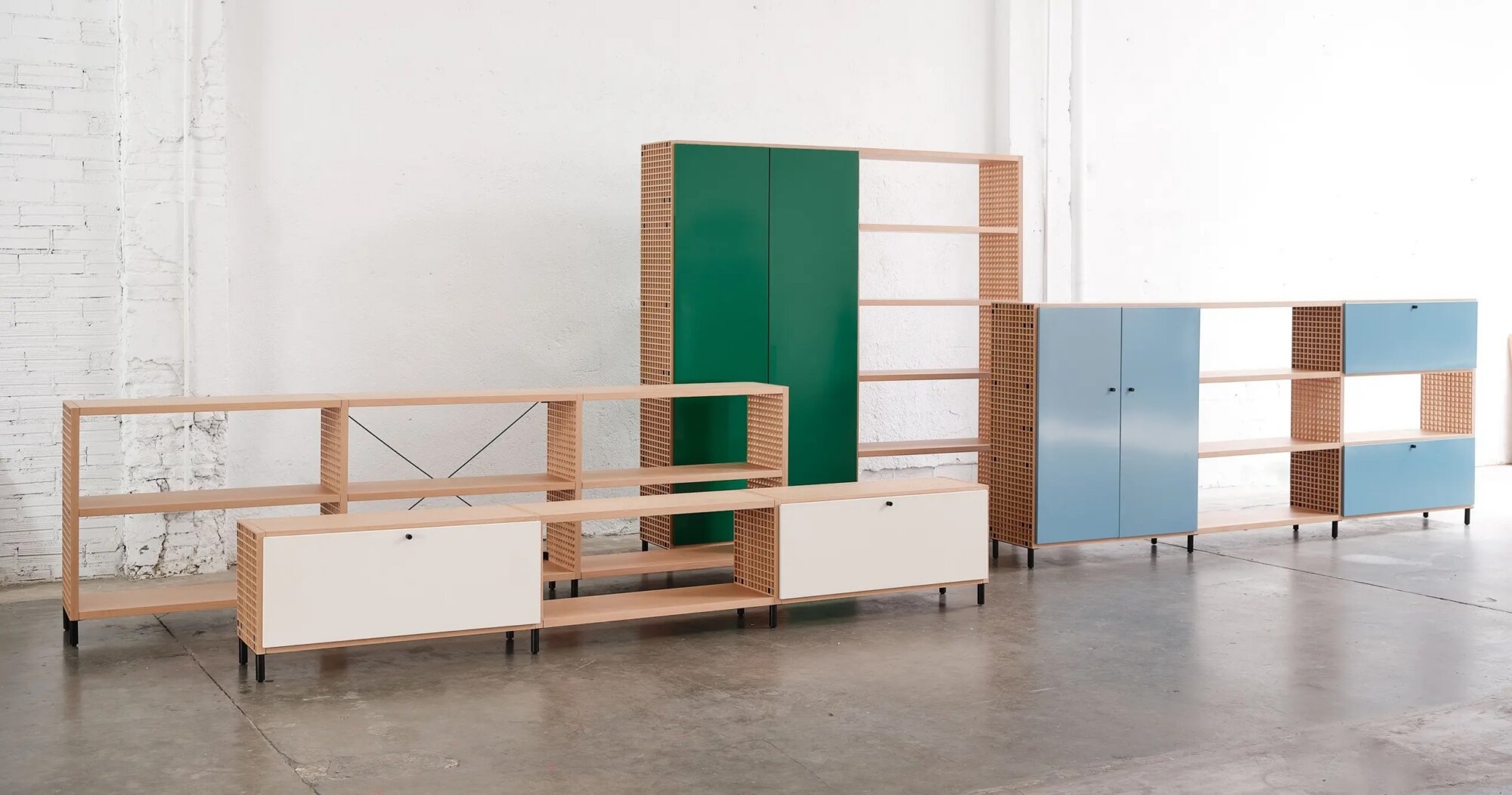 2 | rewire Modular wooden shelving units with cream drawers and green and blue cabinet doors against a white industrial wall.