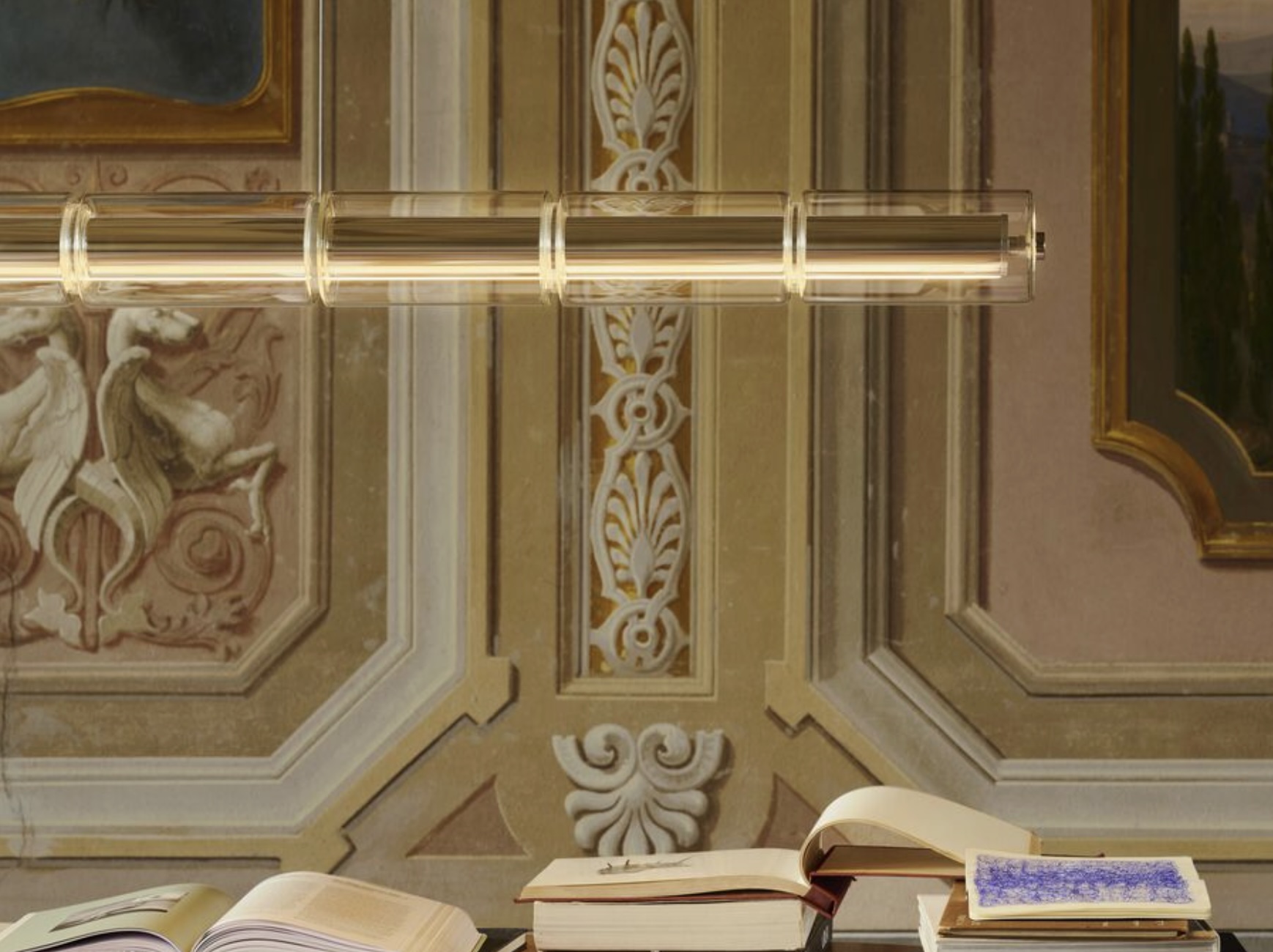 Screenshot | rewire Upside-down view of an ornate ceiling and wall panels with a desk of open and stacked books in the foreground.