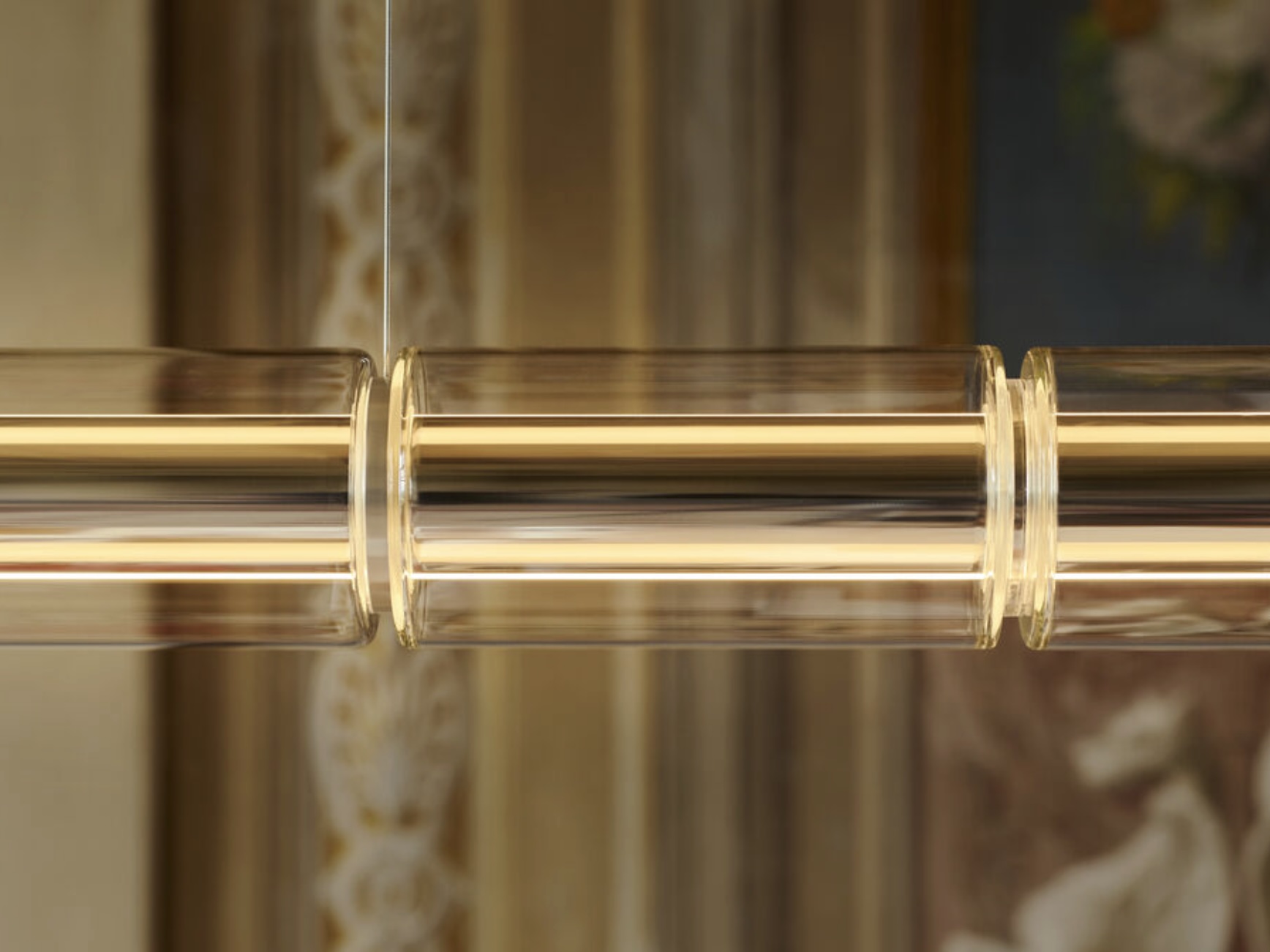 Screenshot | rewire Close-up of a gold-tone cylindrical glass pendant or tubing with metal joints, part of a modern light fixture or railing.