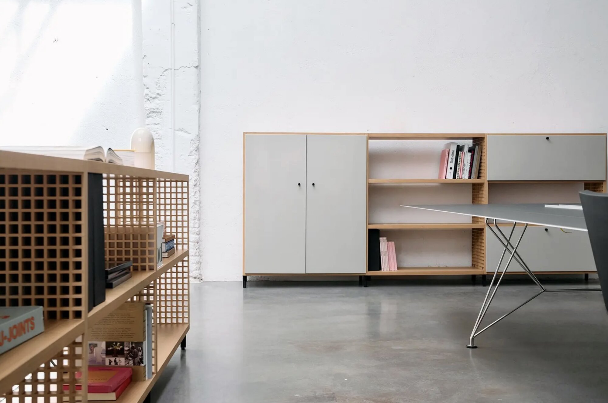 Screenshot | rewire Minimalist office scene with light wood shelving, a gray cabinet, and a glass-top table against a white, textured wall