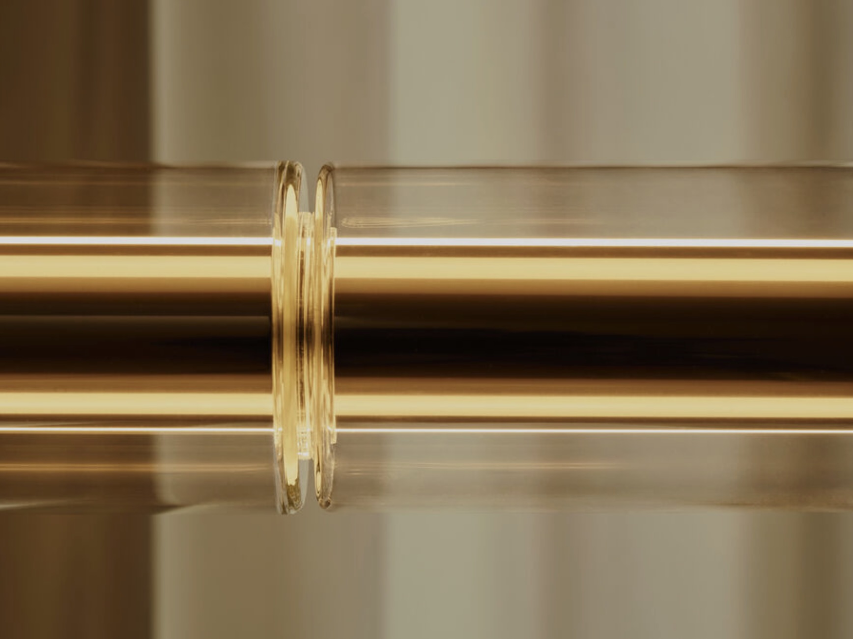 Screenshot | rewire Close-up of two clear glass rings around a shiny metallic rod with warm golden lighting in the background.