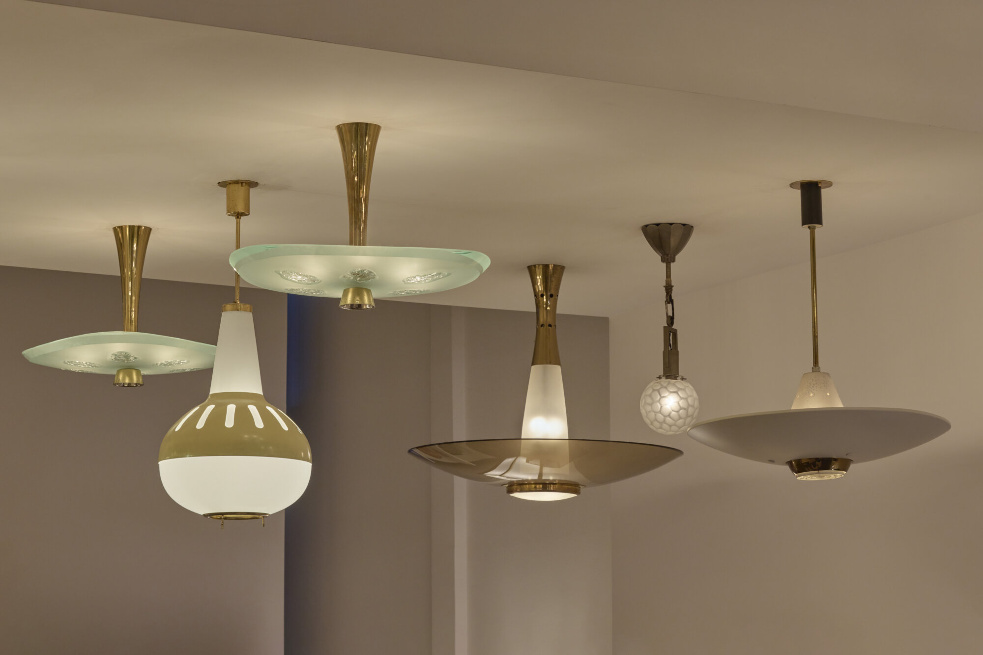Several mid-century modern pendant lamps hanging from a ceiling in a showroom.