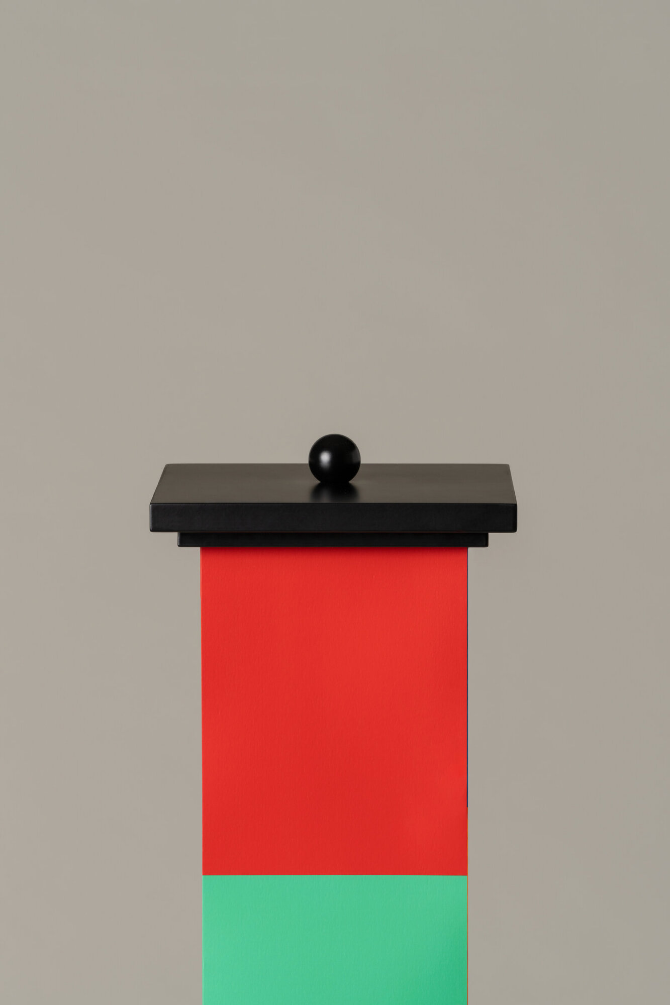La-bella-durmiente-enric-badrinas-2024-22-det-x2400 | rewire Abstract sculpture: black ball perched on a black rectangular platform atop a tall red column with a green base against a neutral background.