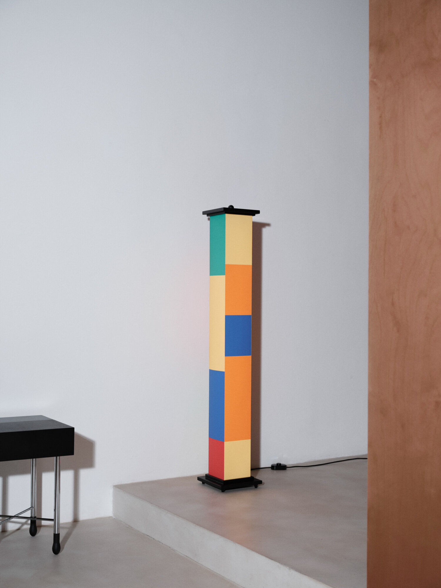 La-bella-durmiente-menor-coke-bartrina-vasto-2025-1560-x2400 | rewire Tall sculpture made of stacked colored blocks (teal, yellow, orange, blue, red) on a black base, displayed in a gallery.