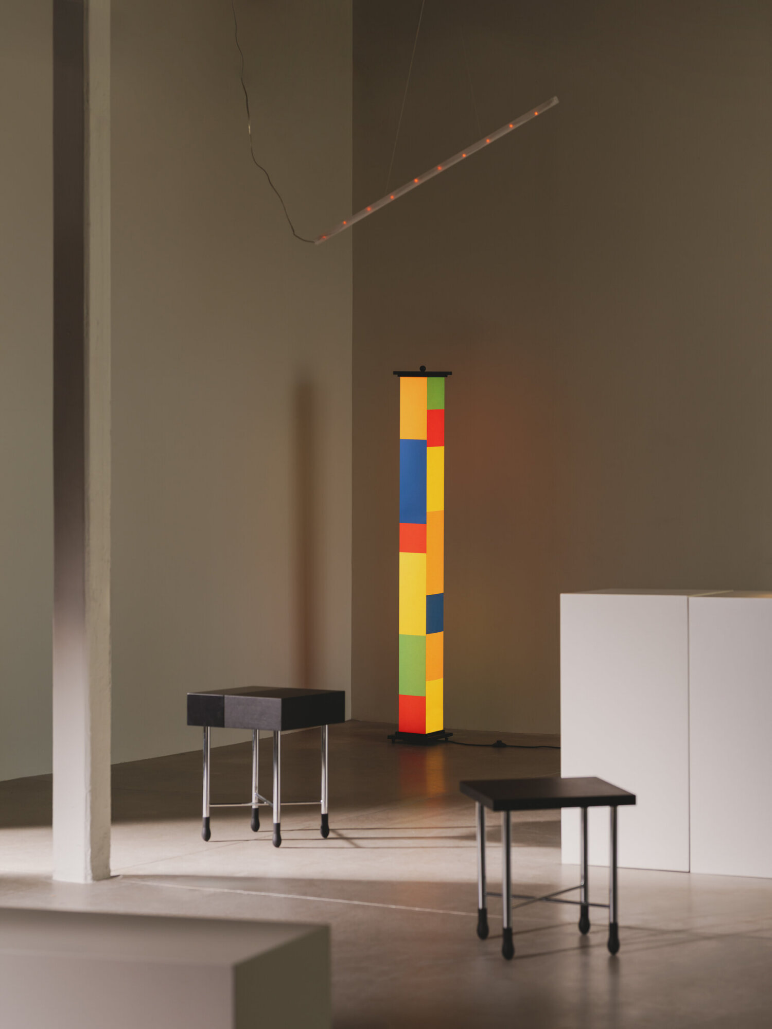 La-bella-durmiente-mesita-go-la-colilla-euroluce-enric-badrinas-2025-2402-x2400 | rewire Tall colorful column made of stacked blocks in a gallery, with two stools nearby.