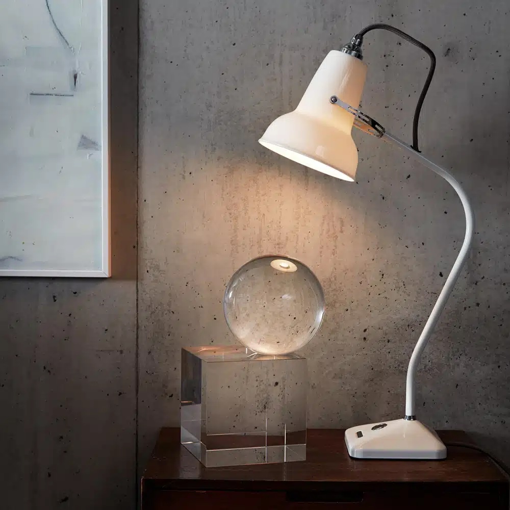 Original_1227_mini_ceramic_table_lampjpg | rewire Modern white adjustable desk lamp casts warm light onto a glass sphere resting on a clear cube on a dark wooden table.