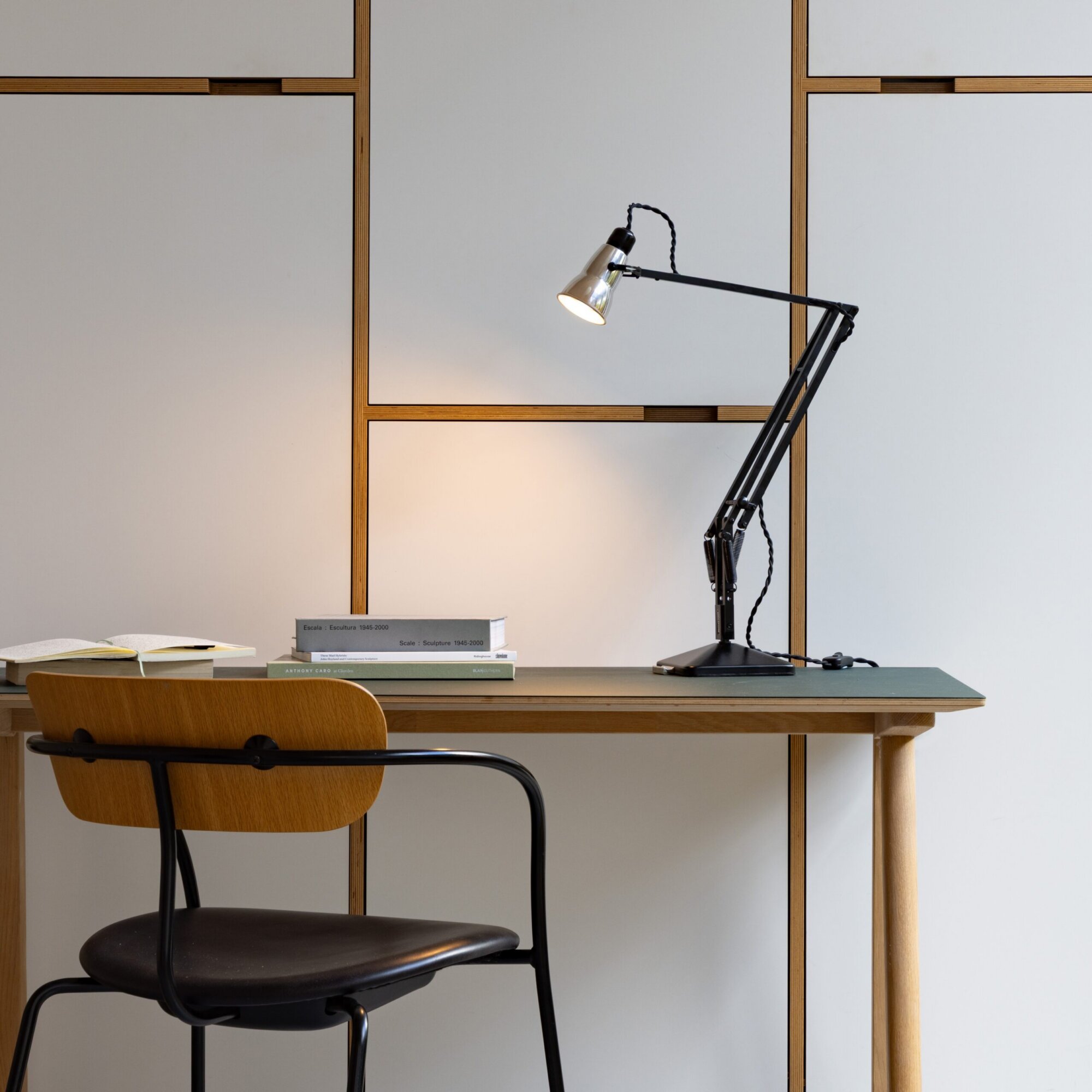 Original-315-desk-lamp-silver-black_2926ls_sq_wh1-1-scaled | rewire A desk with a black adjustable lamp and a stack of books, in a modern room with wooden-framed wall panels behind it.