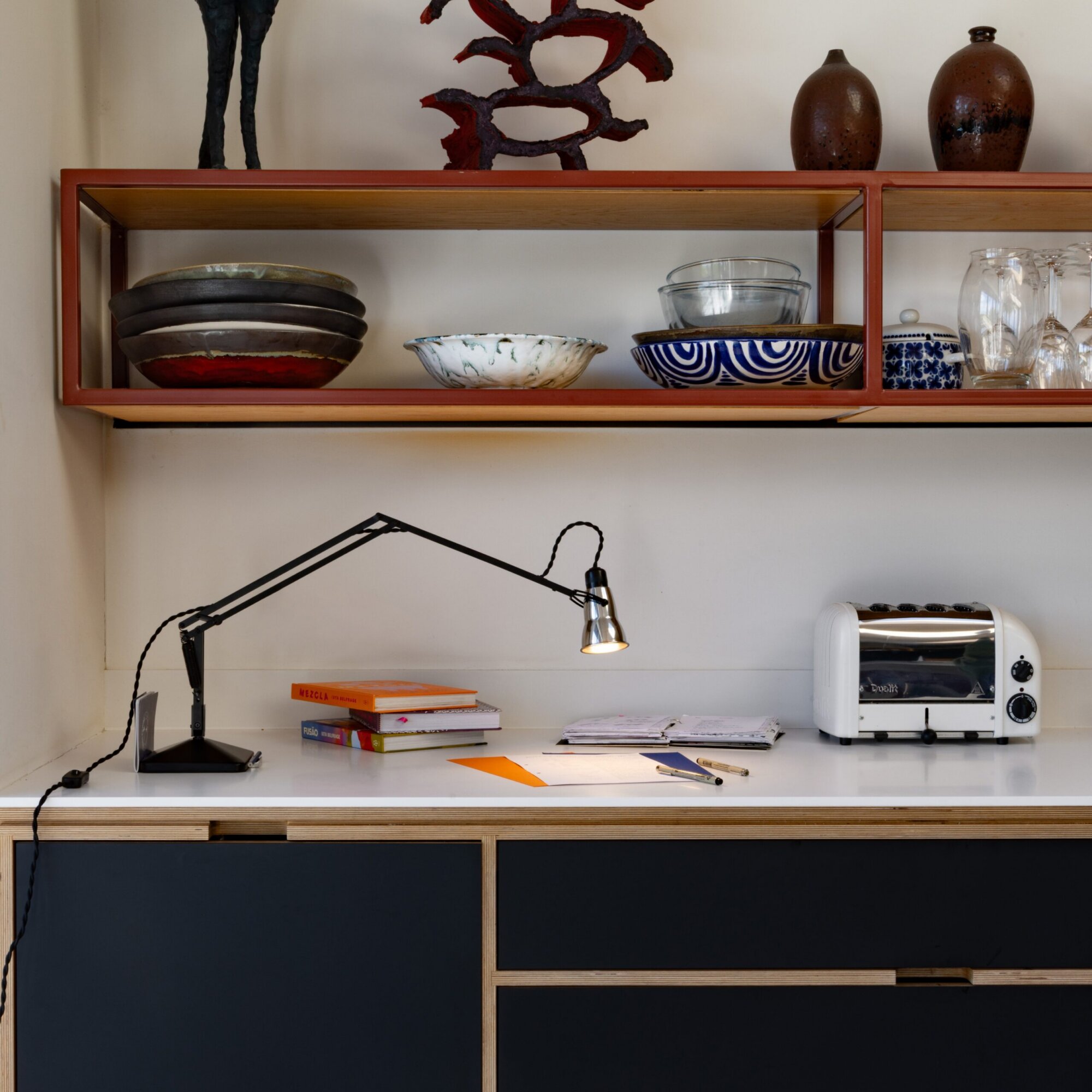 Original-315-desk-lamp-silver-black_2926ls_sq_ws11-scaled | rewire Shelf with ceramic bowls, glassware, and a toaster on a white counter; orange and blue books lie nearby, and a desk lamp extends across the scene.