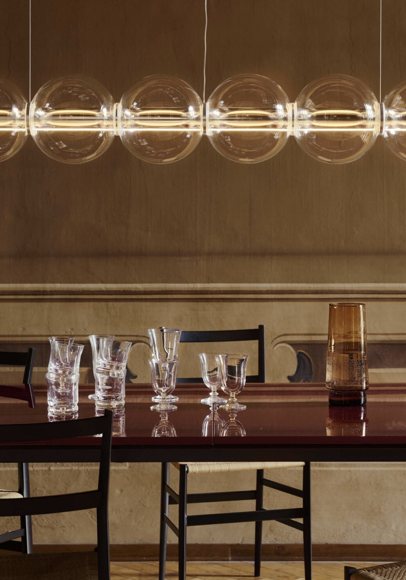 Row of round glass pendant lights hanging above a dining table with glassware and a water carafe in a modern restaurant setting