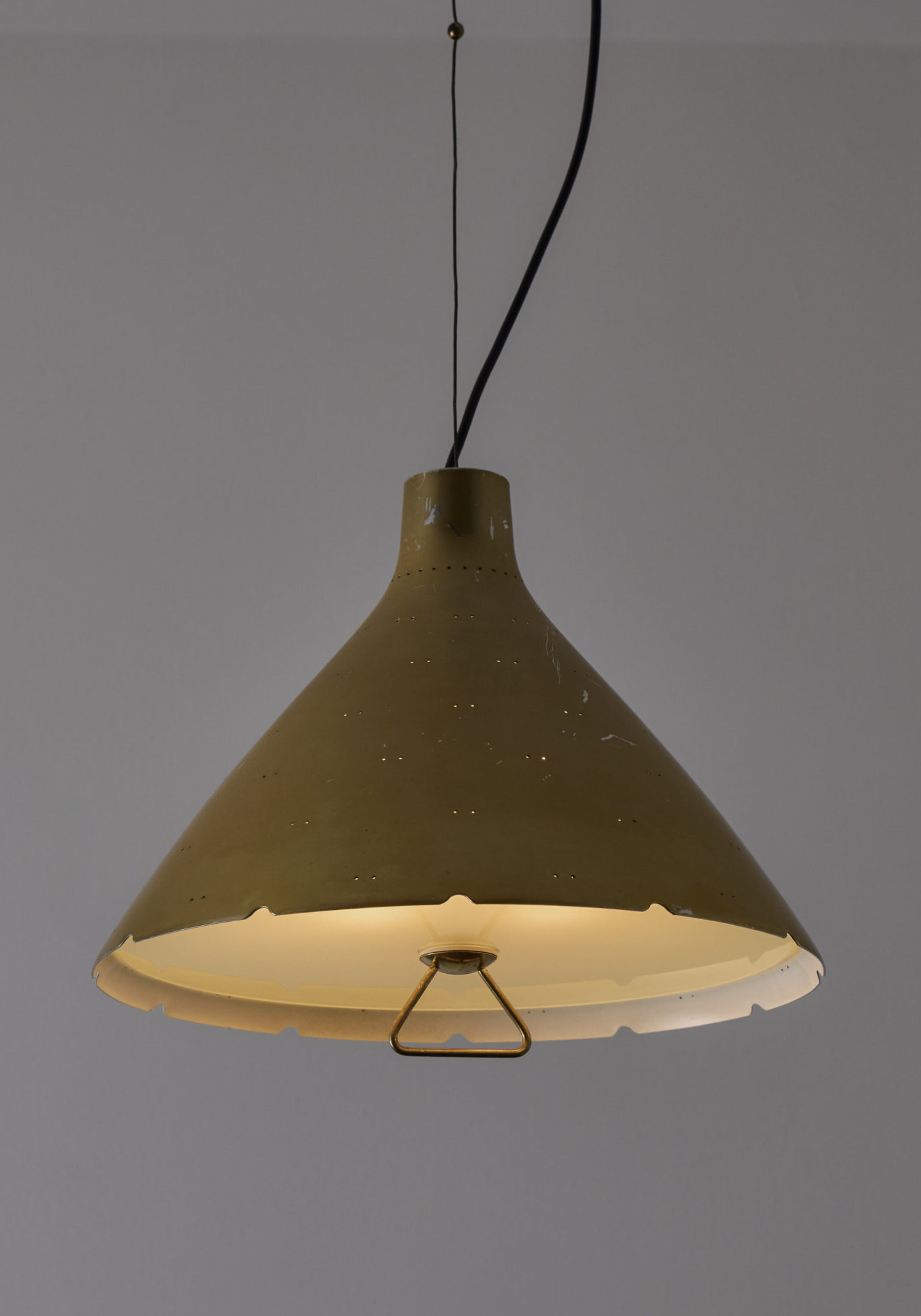 Yellow pendant lamp hanging from a ceiling with black cords against a gray wall.